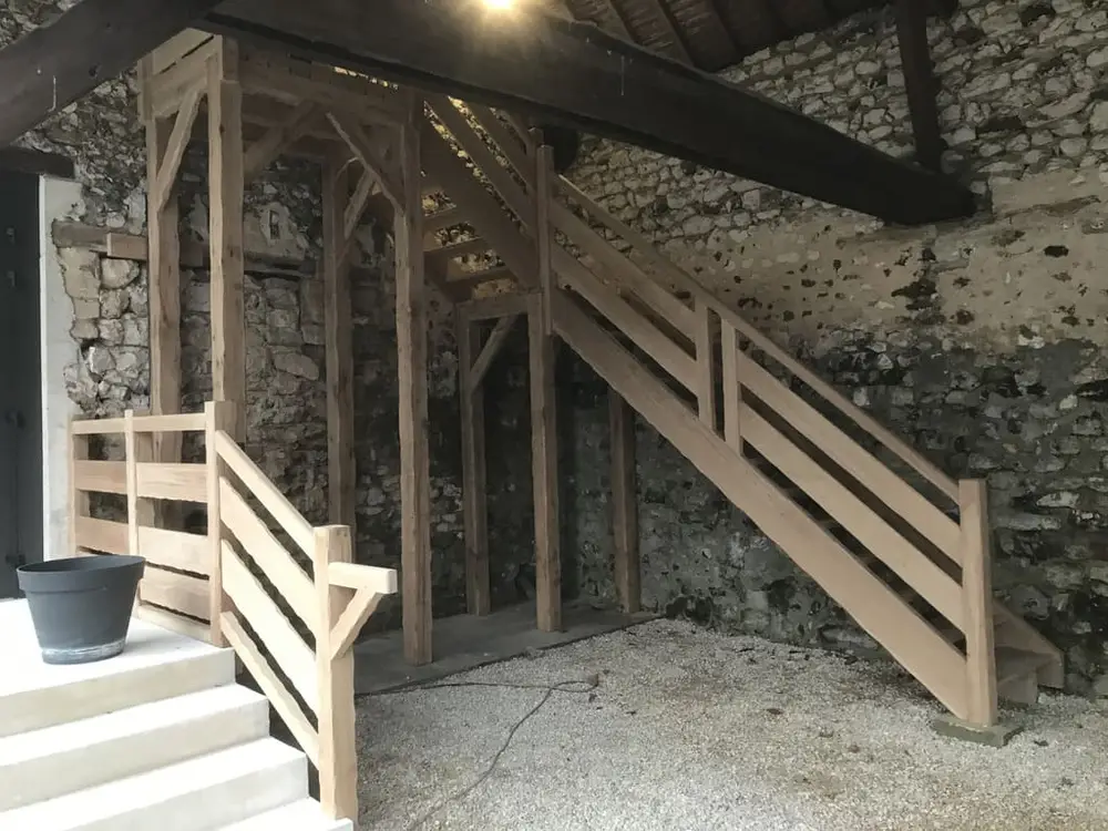 Escalier en bois dans un bâtiment en pierre, mettant en valeur des chênes naturels et une architecture rustique.