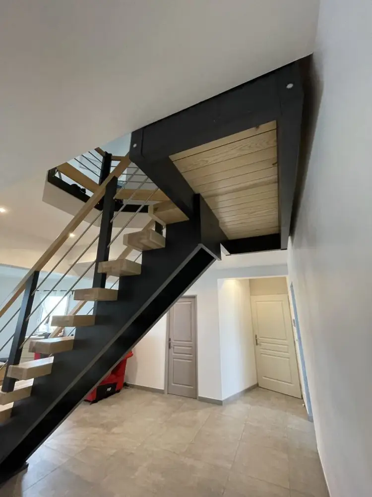 Escalier à double limon central en sapin gris 7016, avec des marches en frêne vitrifié et des rampes en métal noir.