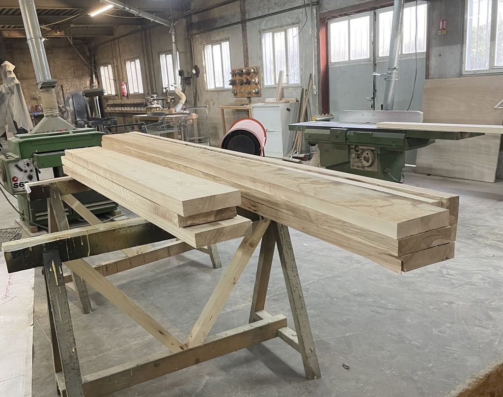 Atelier de menuiserie avec une grande quantité de bois, incluant des pièces de frêne en cours de transformation.