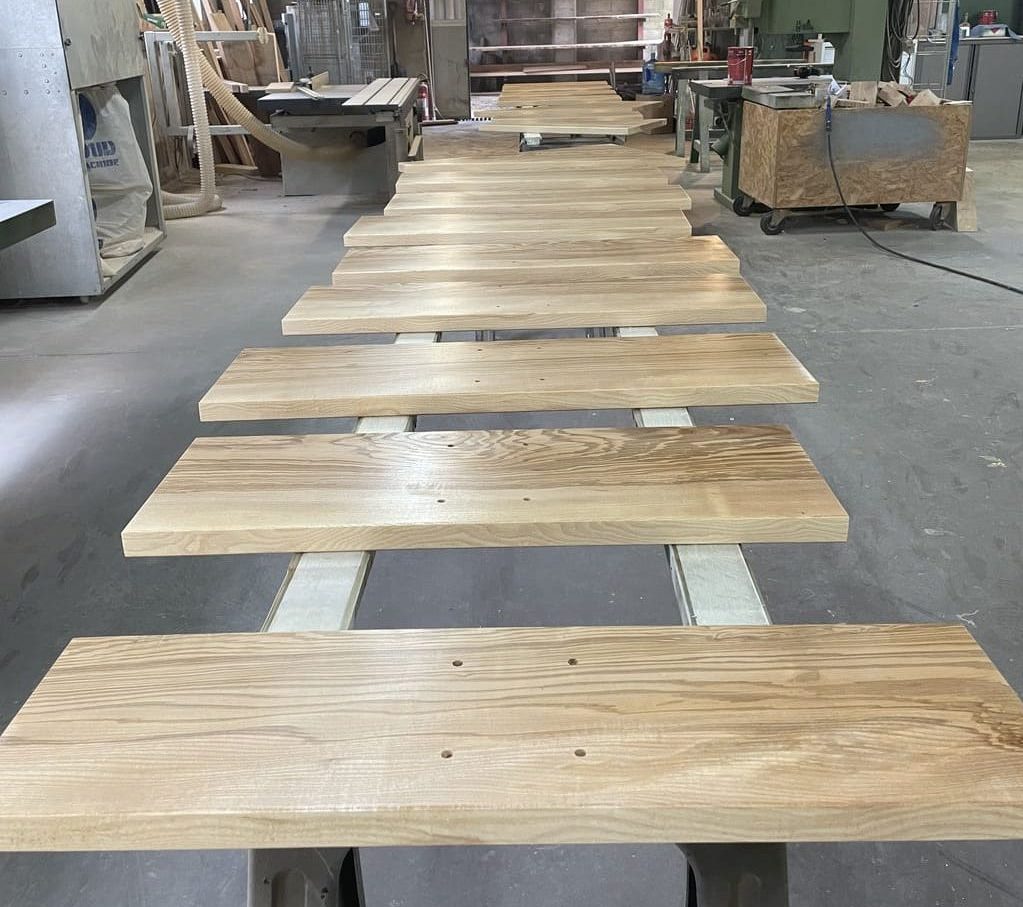 Table en bois massif dans un atelier, entourée de marches en cours de vitrification.