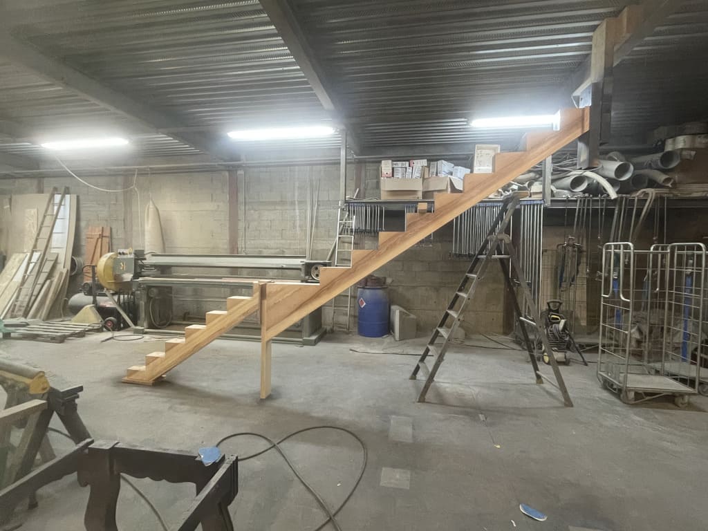 Escalier en bois dans un atelier, avec une échelle à côté, prêt à être peint.