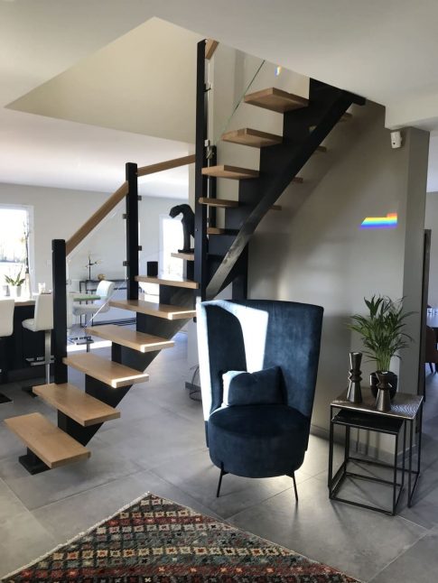 Salon moderne avec un escalier quart tournant noir et des marches en frêne, accompagné d'une chaise élégante.Avec du remplissage en verre
